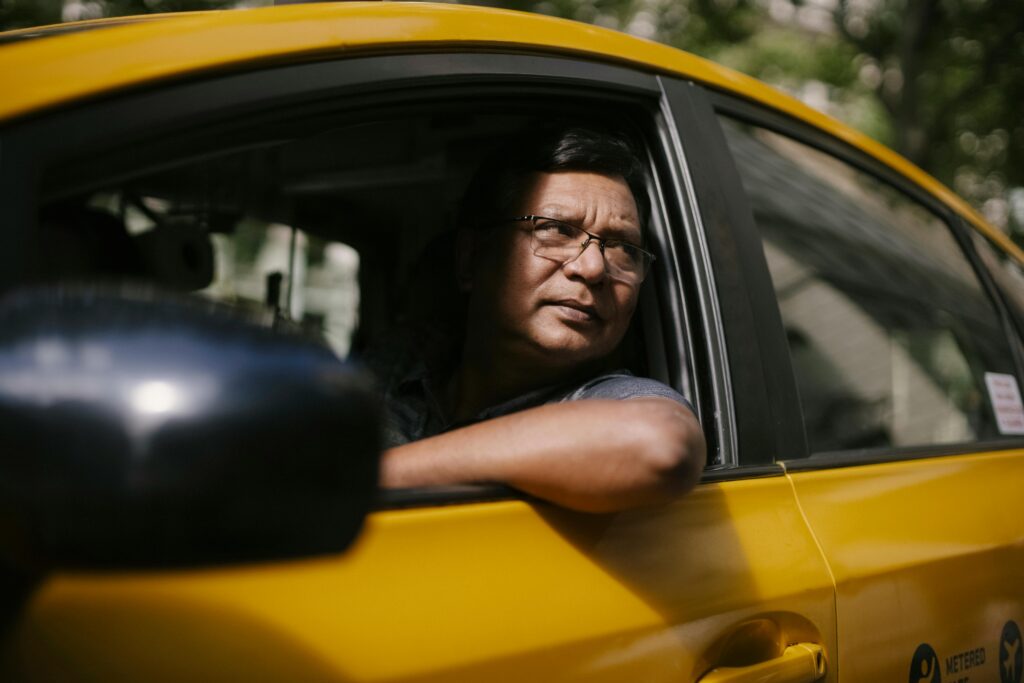 A taxi driver gazes pensively out of his cab window while waiting at a city stop.